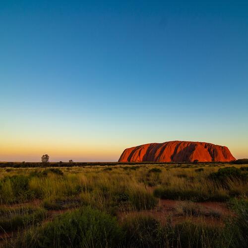 De avond valt boven de roodbruine rotsheuvel Uluṟu in Australië