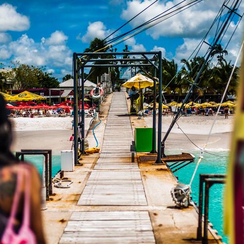 Een steiger aan een strand vol parasols op Barbados