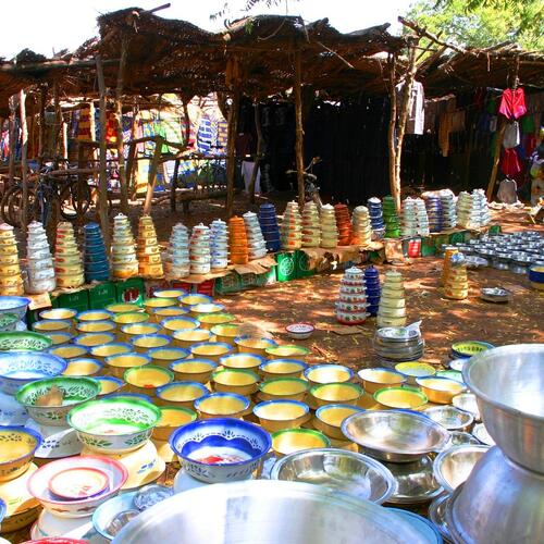 Felgekleurde kommen en potten bedekken de grond op een markt met houten kraampjes in Burkina Faso