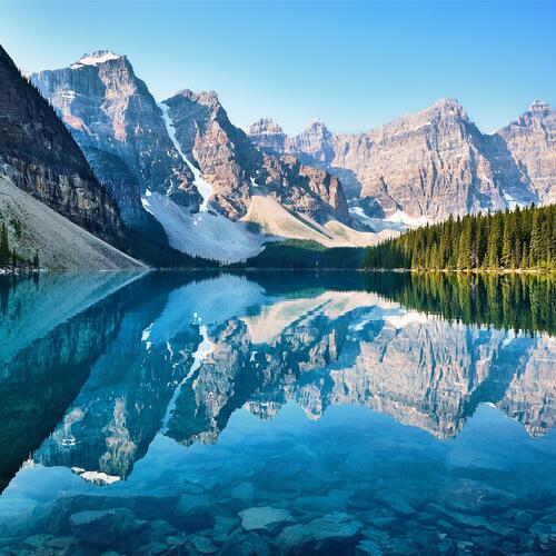 De bergtoppen en naaldbomen reflecteren in het heldere water van Moraine Lake in Canada