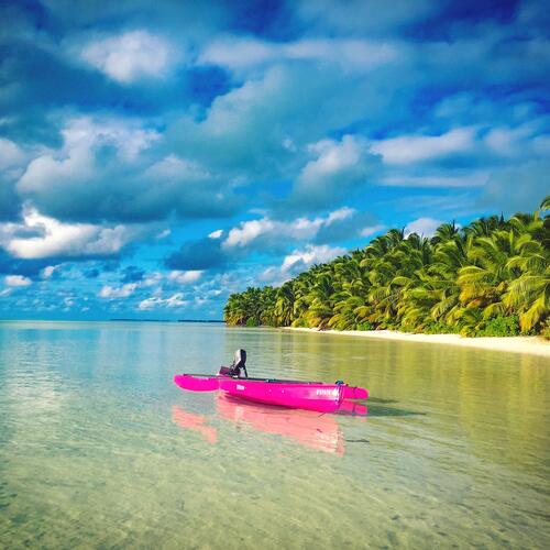 Een felroze kano ligt in het water aan een strand met palmbomen op South Island in de Cocoseilanden