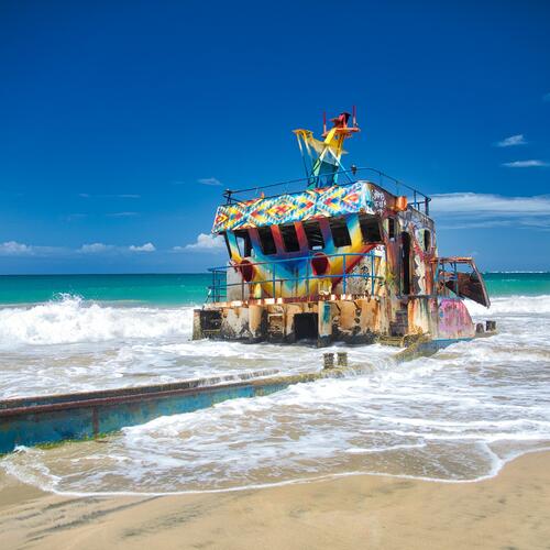 Een verroest en in felle kleuren geschilderd scheepswrak op het strand van Limón in Costa Rica