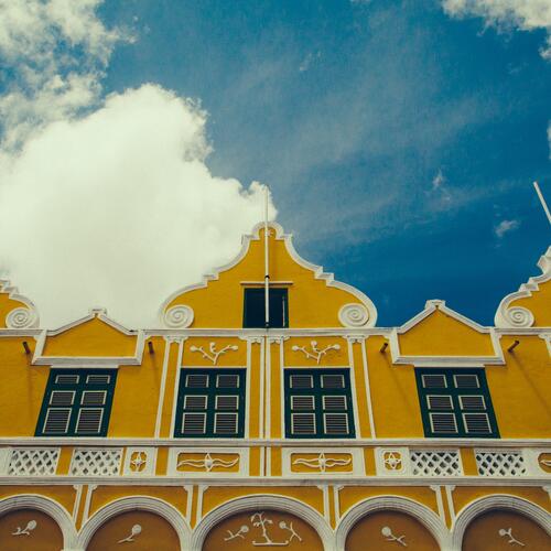 Wolken en een blauwe lucht boven de felgele gedecoreerde koloniale gevels in Willemstad, Curaçao