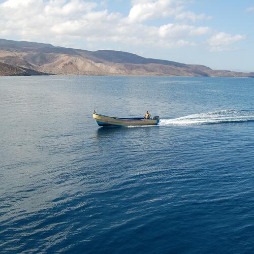 Een visser in een gele motorboot vaart voorbij de heuvelachtige kust van Djibouti