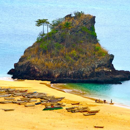 Bootjes liggen op het strand bij een grote rots in de zee op het eiland Annobón in Equatoriaal Guinea
