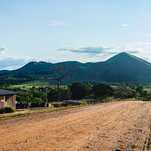 Een houten huisje staat langs een zandweg met op de achtergrond een grote heuvel nabij Lopé, in Gabon