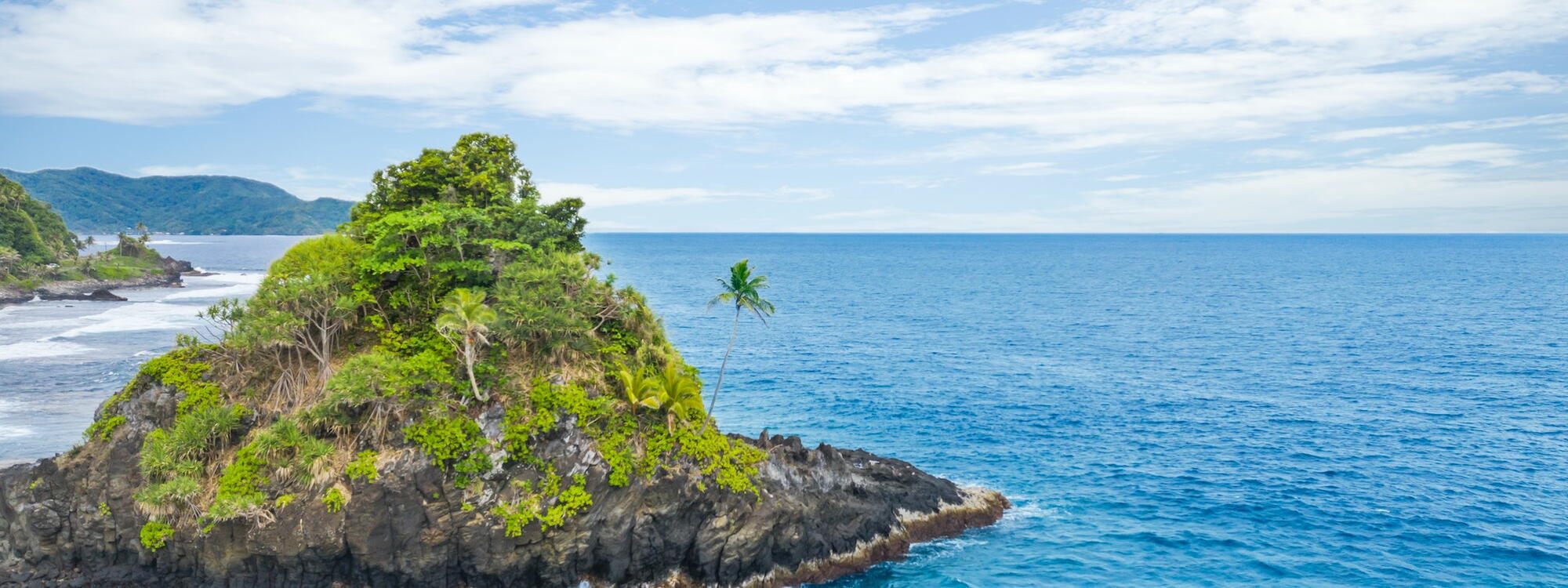 Een rots met palmbomen in de zee aan de kust bij Alega in Amerikaans Samoa