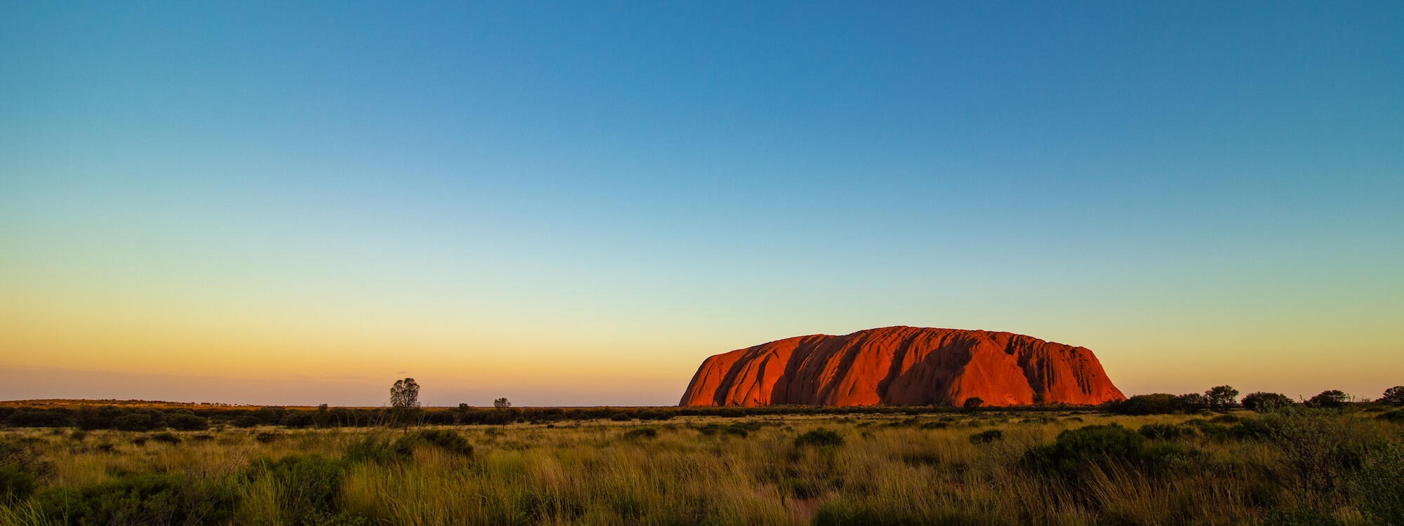 De avond valt boven de roodbruine rotsheuvel Uluṟu in Australië