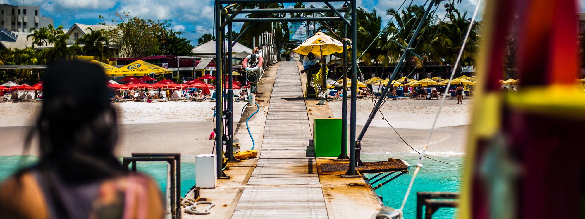 Een steiger aan een strand vol parasols op Barbados
