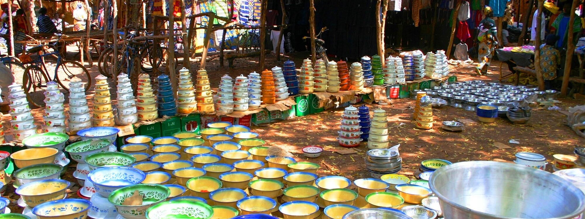 Felgekleurde kommen en potten bedekken de grond op een markt met houten kraampjes in Burkina Faso