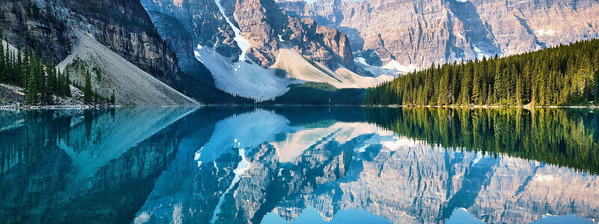 De bergtoppen en naaldbomen reflecteren in het heldere water van Moraine Lake in Canada