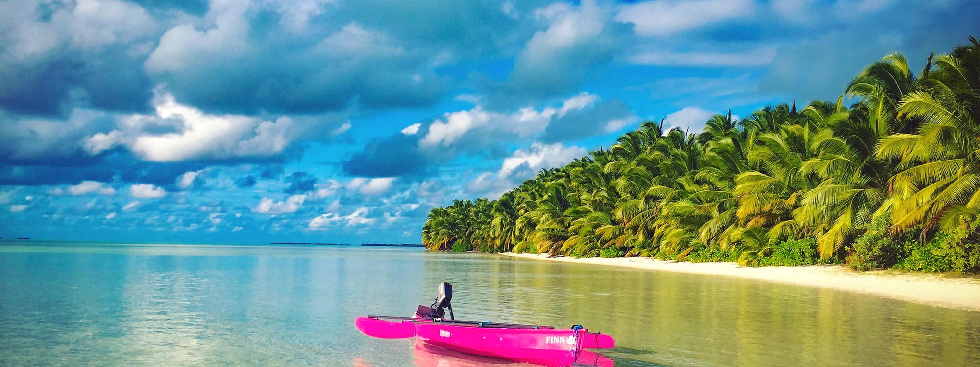 Een felroze kano ligt in het water aan een strand met palmbomen op South Island in de Cocoseilanden