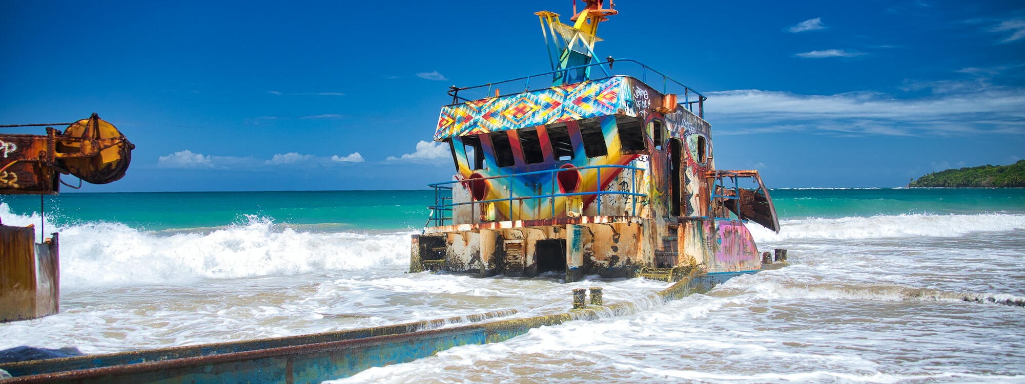 Een verroest en in felle kleuren geschilderd scheepswrak op het strand van Limón in Costa Rica