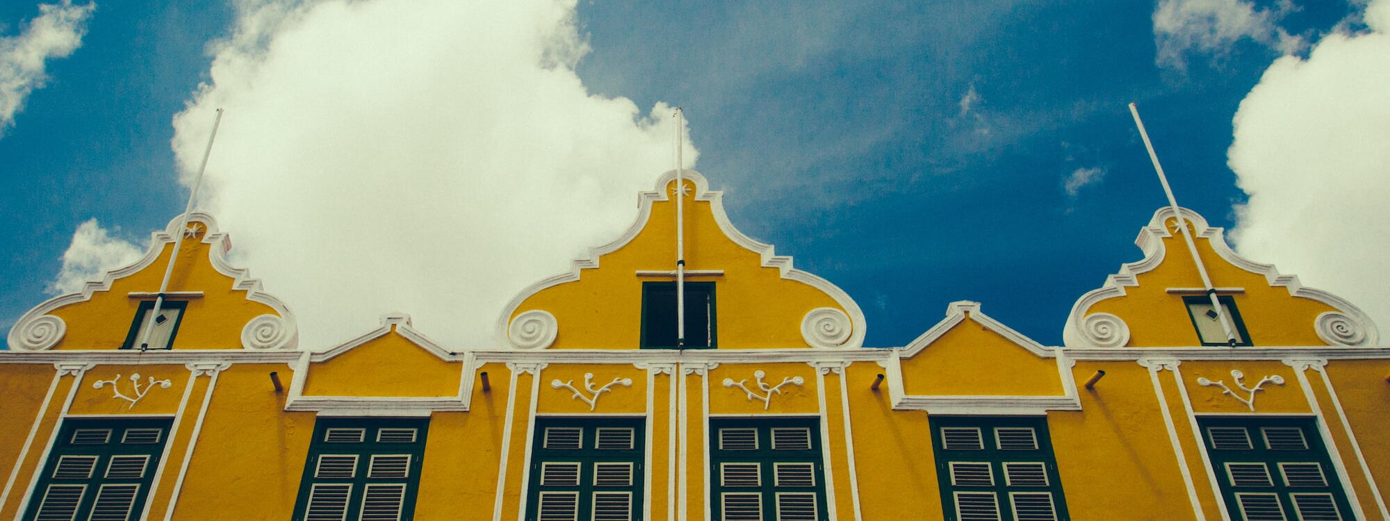 Wolken en een blauwe lucht boven de felgele gedecoreerde koloniale gevels in Willemstad, Curaçao