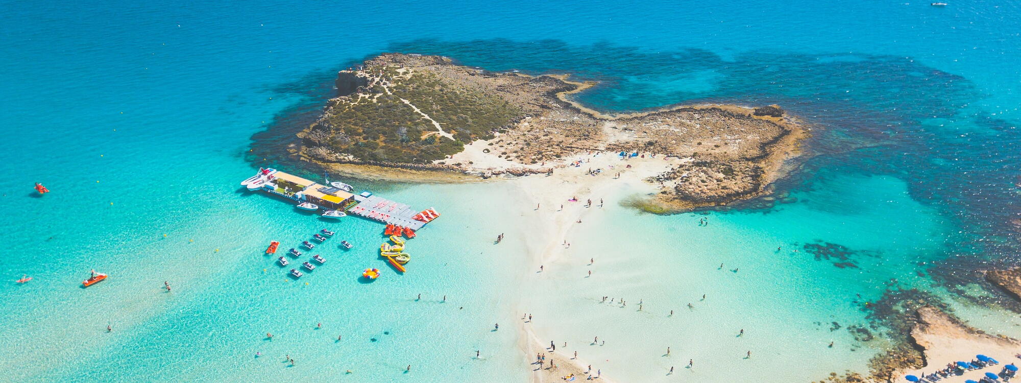 Een strand bedekt door blauwe parasols loopt uit op een eiland in Ayia Napa in Cyprus