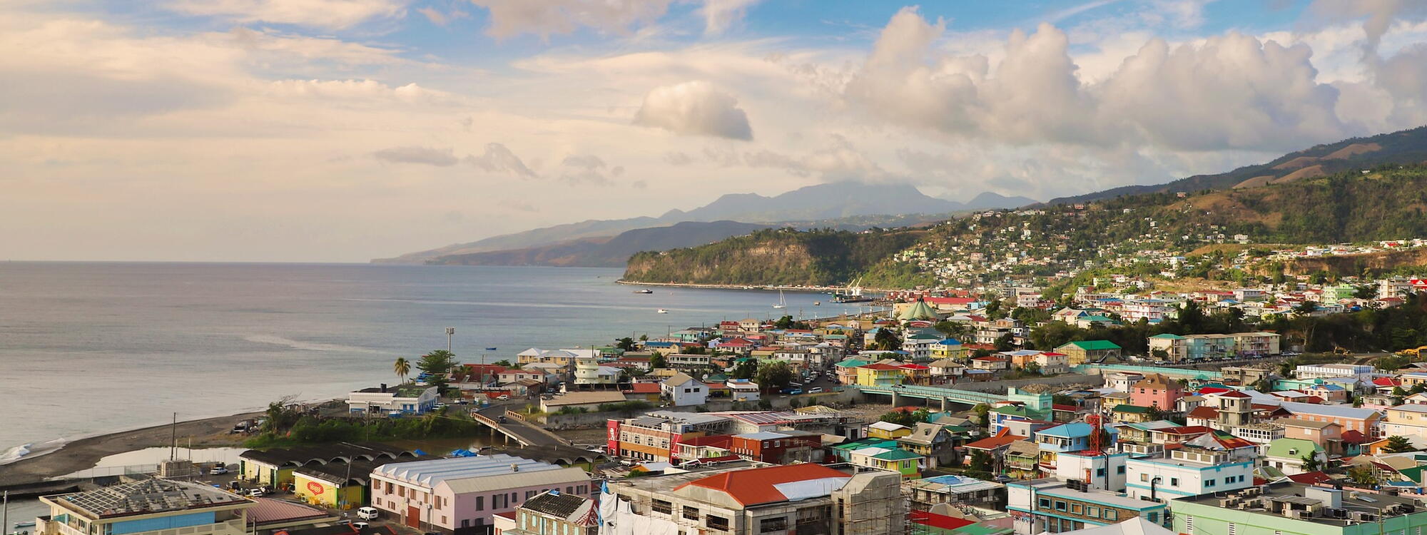 Een luchtfoto van de gekleurde huizen in Roseau, de hoofdstad van Dominica, met de zee en de bergen in de achtergrond