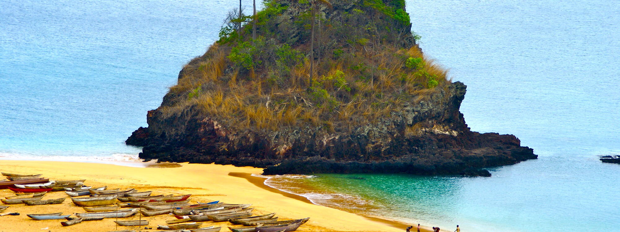 Bootjes liggen op het strand bij een grote rots in de zee op het eiland Annobón in Equatoriaal Guinea