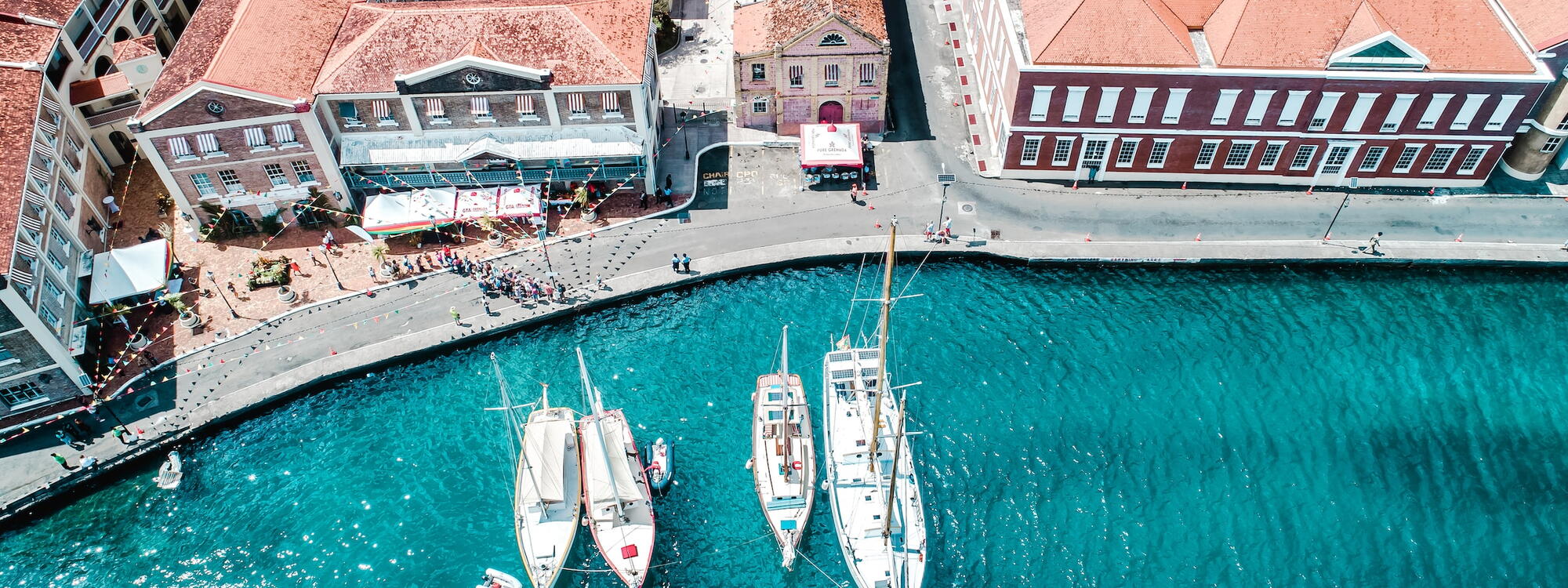 Boten liggen langs een kade met vlaggetjes boven de straat en Georgiaanse gebouwen in Saint George