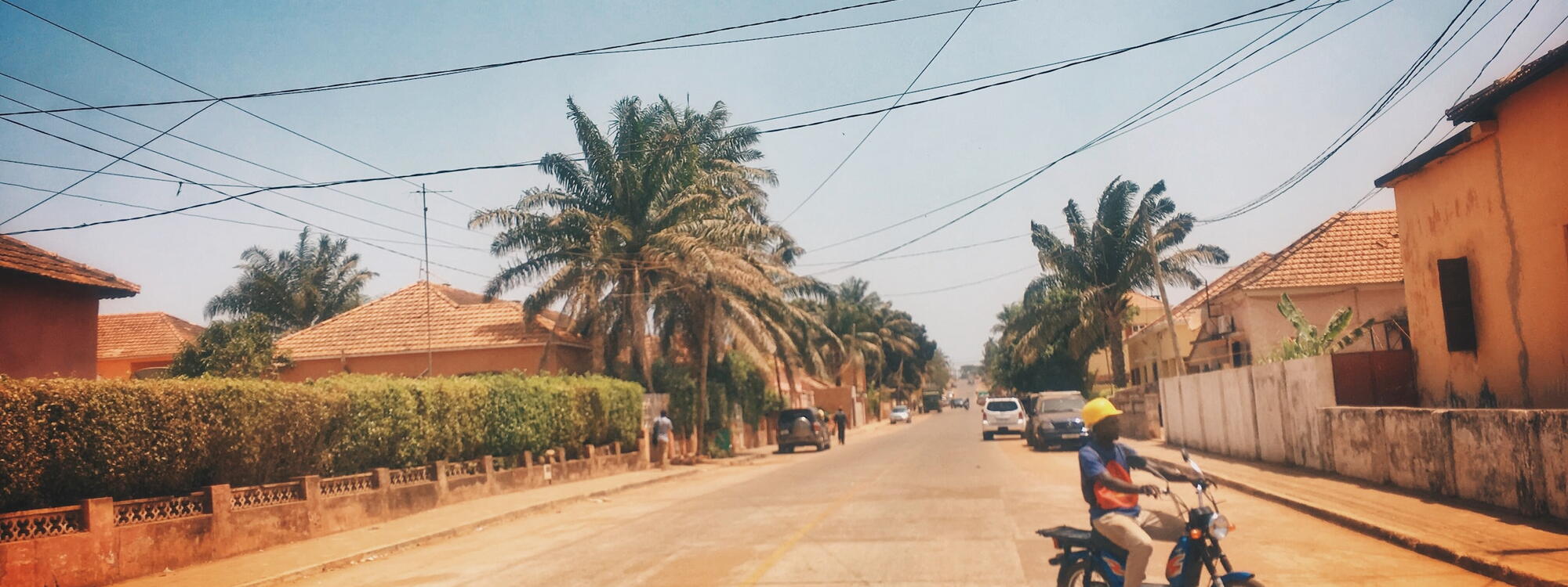 Een man rijdt op een brommer tussen okergele huizen in Bissau