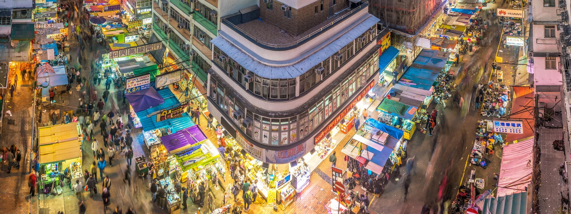 Mensen lopen tussen felgekleurde marktkraampjes in de drukke nachtelijke straten van Sham Shui Po in Hong Kong